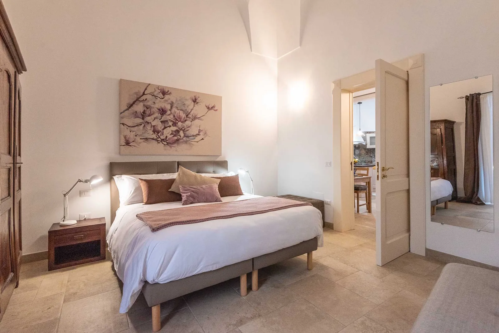 Camera con un letto matrimoniale, decorata con un quadro di fiori e un armadio in legno. Una porta conduce a un'altra stanza