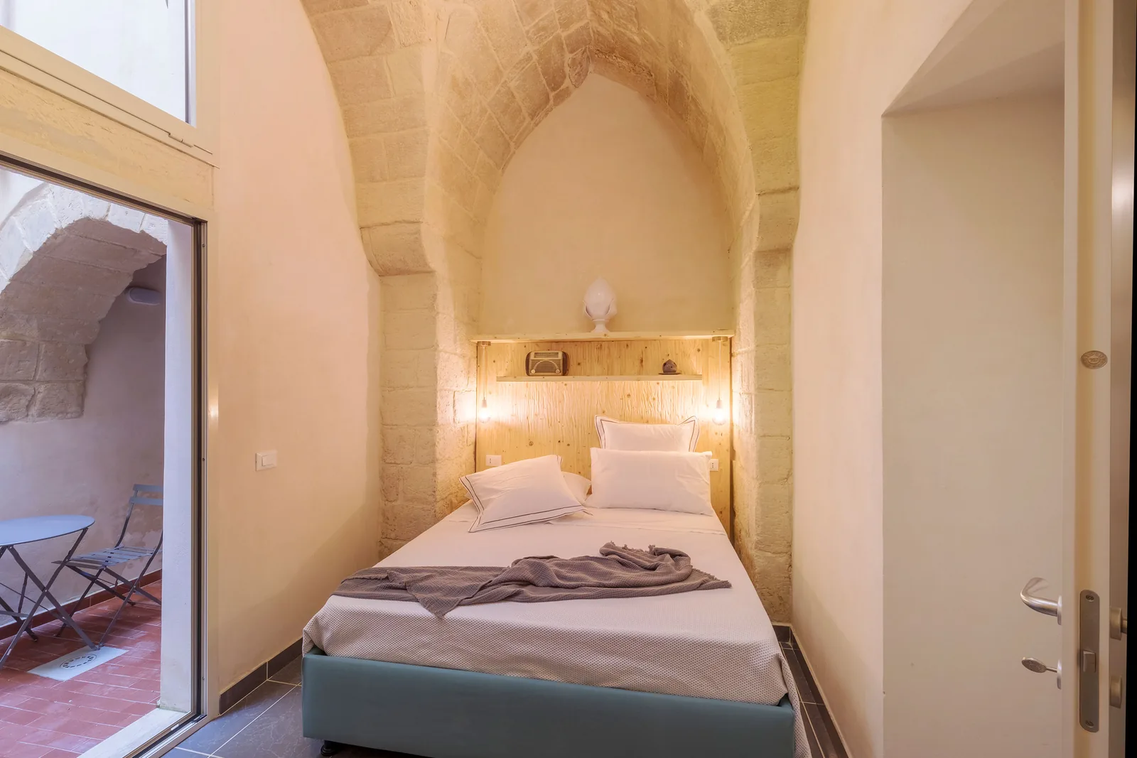 Camera da letto con letto matrimoniale, pareti in pietra e luci soffuse, accesso a un piccolo balcone
