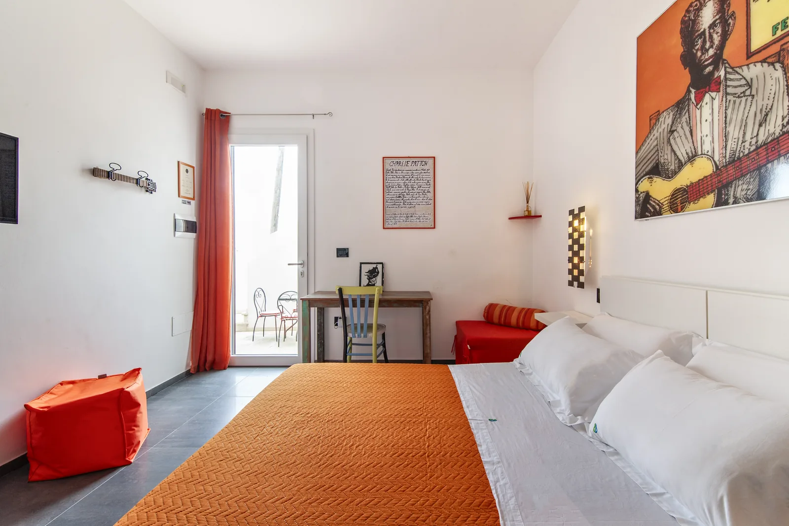 Camera da letto con un letto matrimoniale, un tavolo, una sedia colorata e un'illustrazione di un musicista