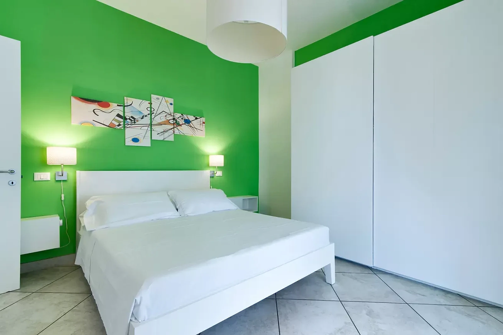 Camera da letto con parete verde, letto bianco, lampade e un'opera d'arte astratta appesa