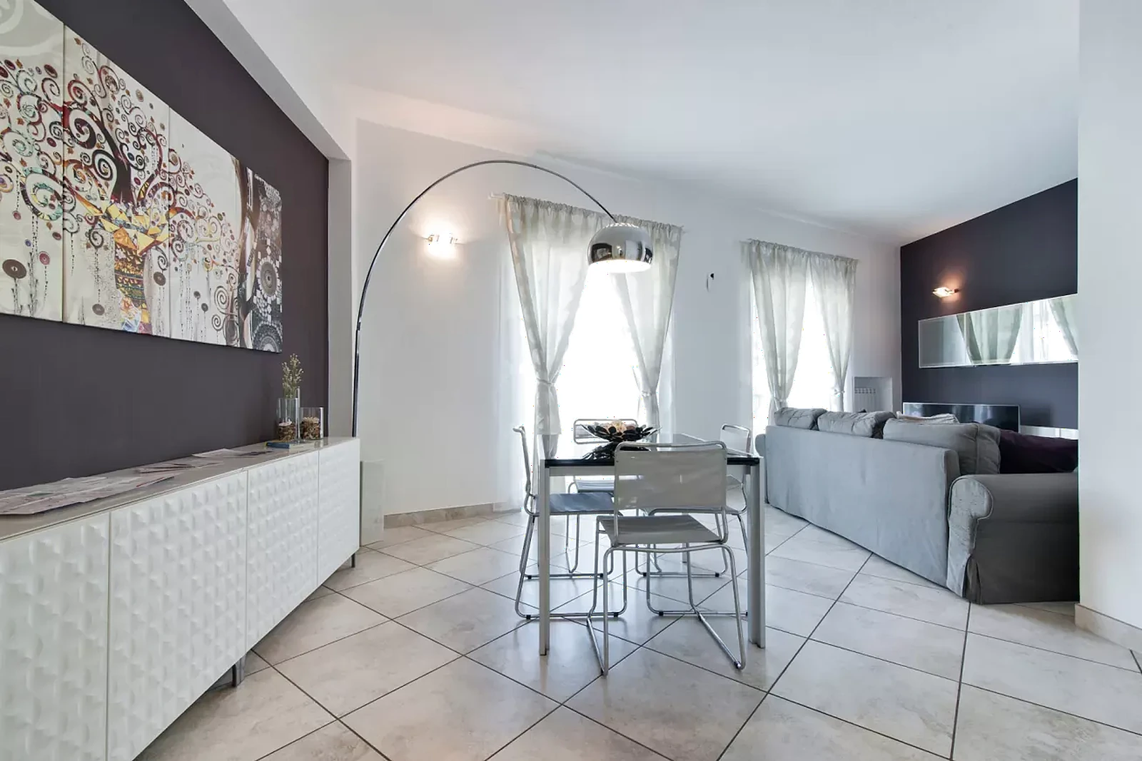 Interno di un soggiorno moderno con un tavolo da pranzo e sedie, un divano grigio e una decorazione artistica sulla parete