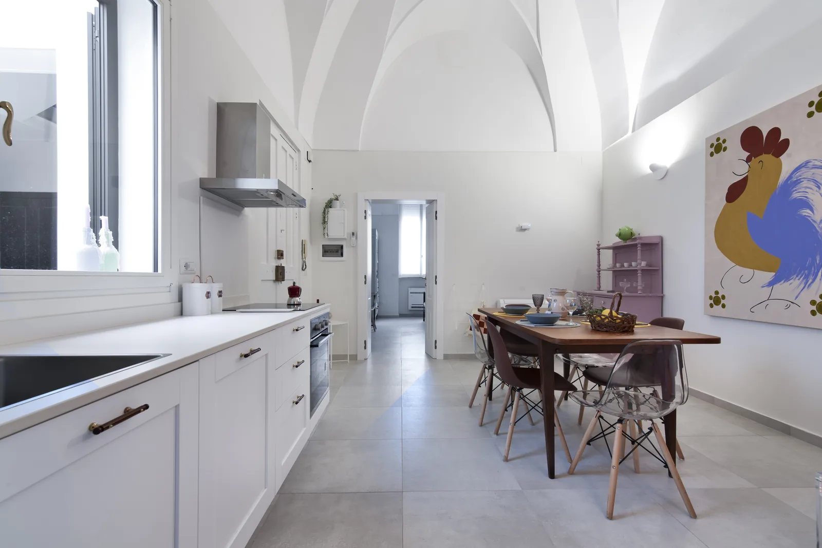 Una cucina moderna con soffitto a volta, un tavolo da pranzo in legno e una grande opera d'arte di un gallo sulla parete