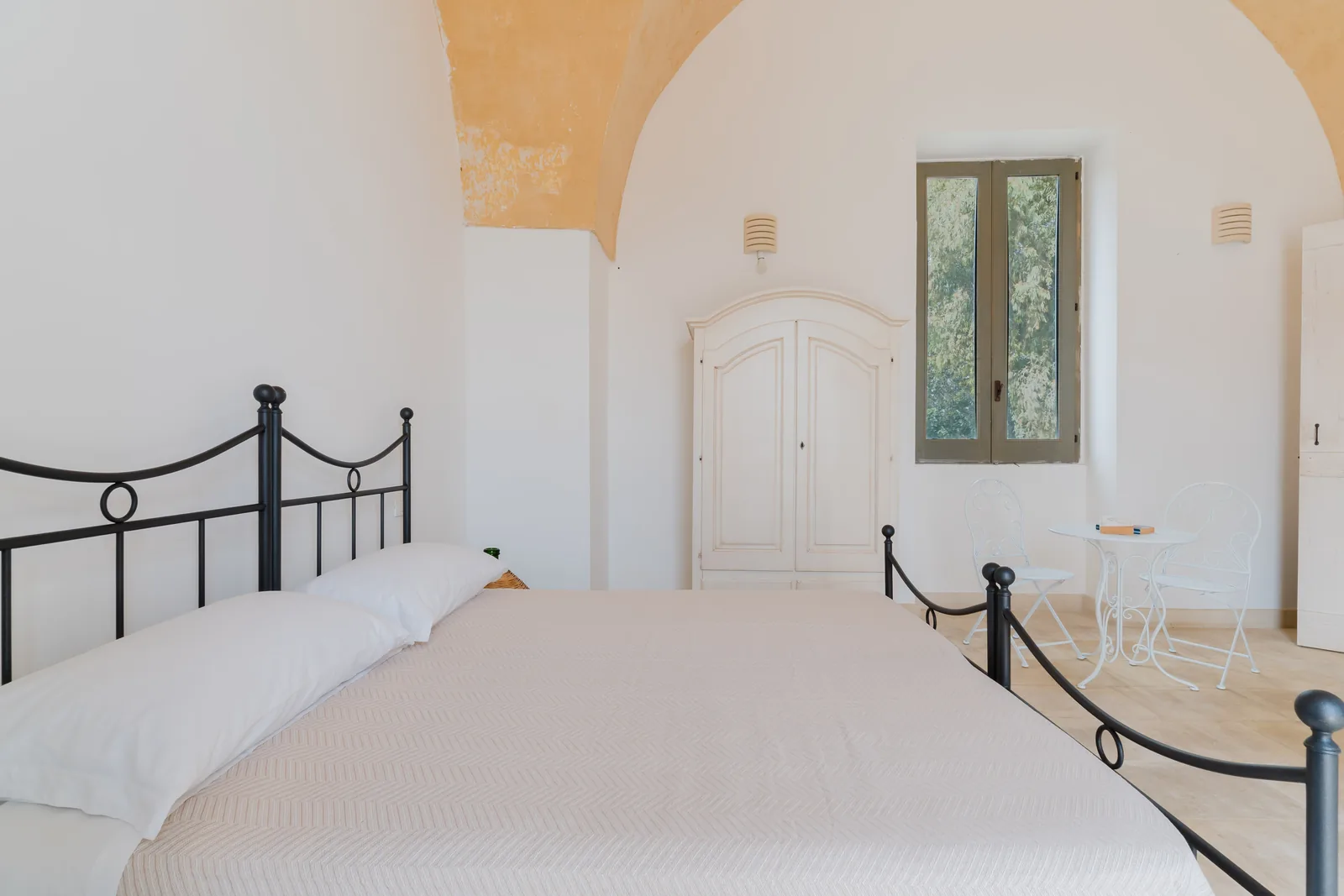 Camera da letto con letto matrimoniale, armadio bianco e tavolo con sedie bianche vicino alla finestra