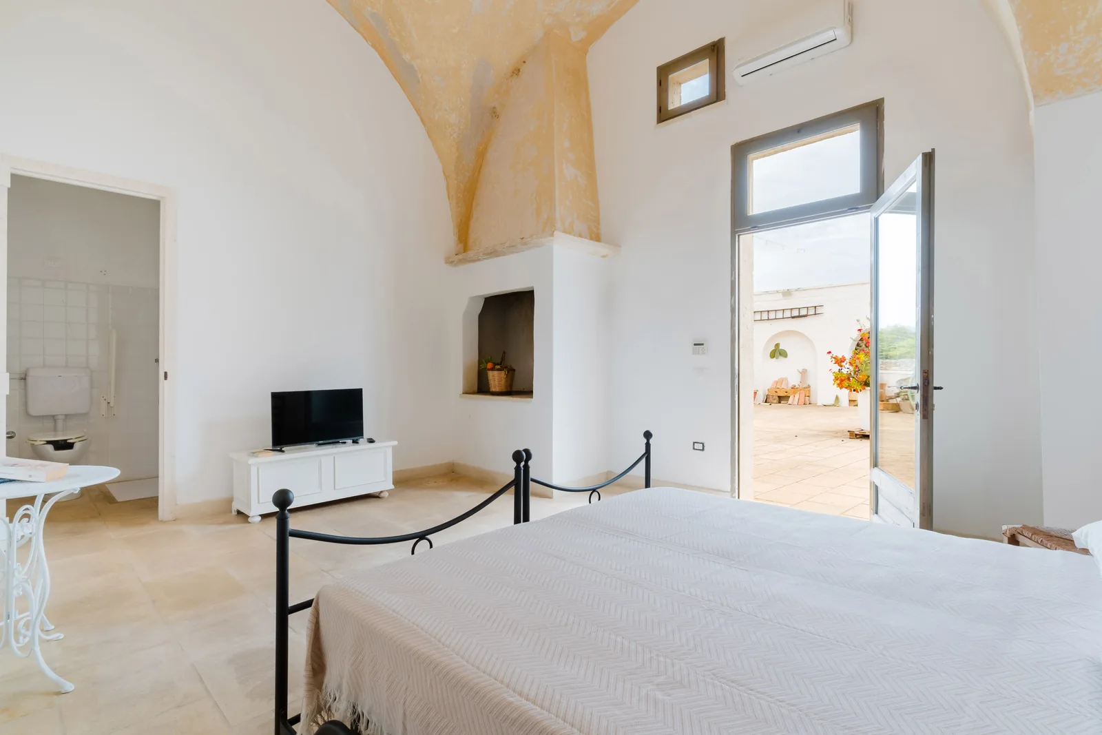 Camera da letto luminosa con letto matrimoniale, TV e porta che si apre su un patio esterno