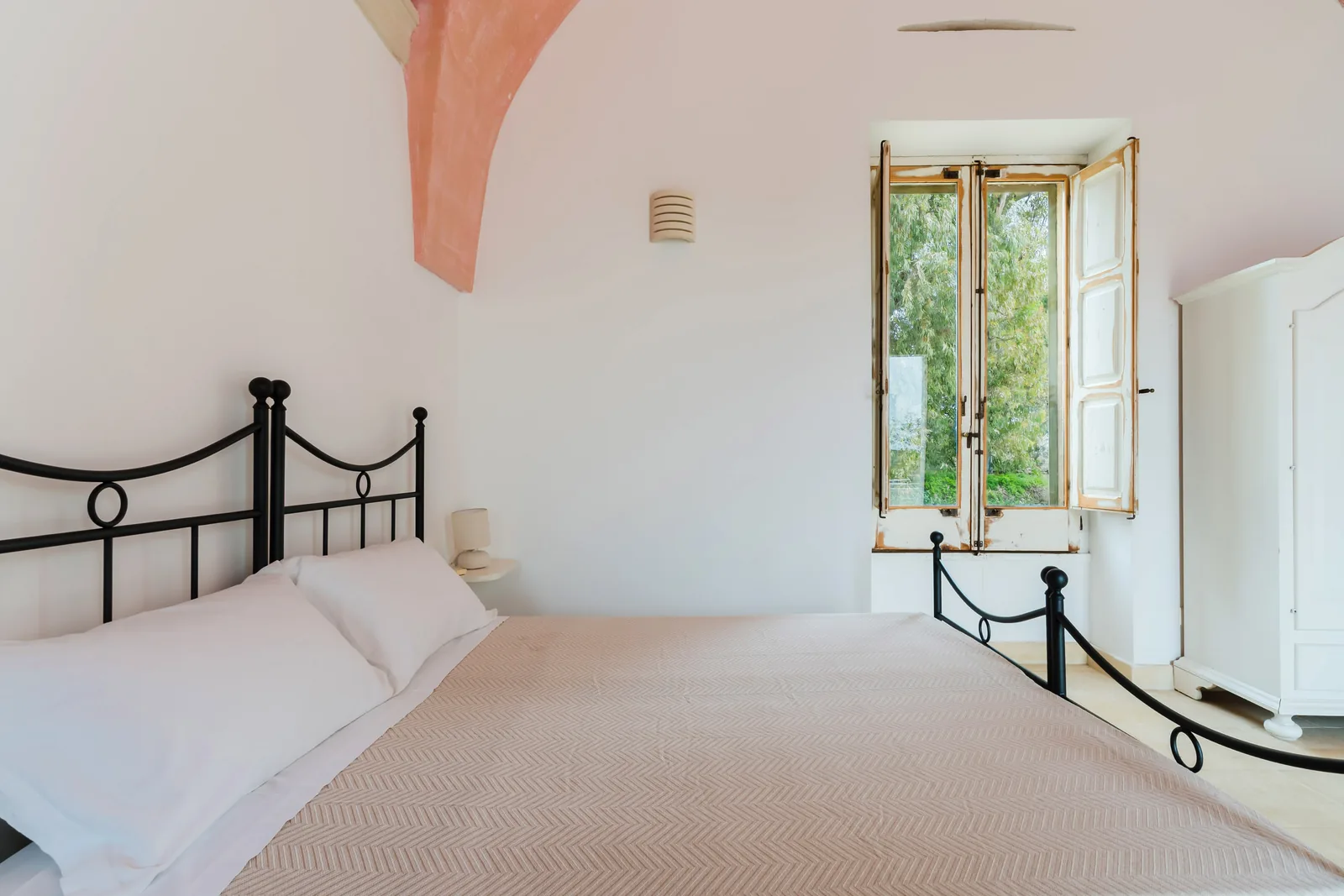 Camera da letto con un letto matrimoniale, pareti bianche e una finestra aperta che dà su un giardino
