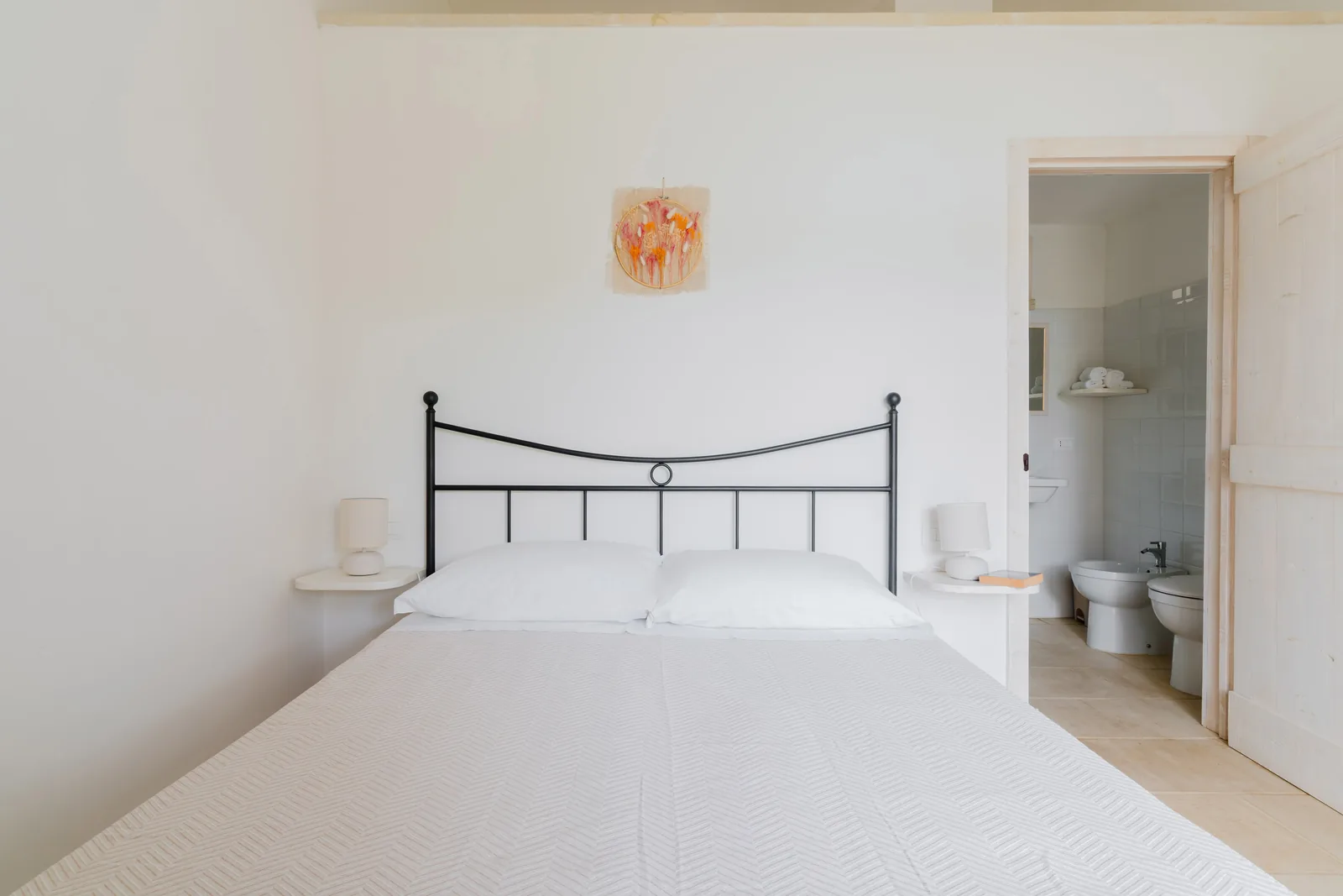 Camera da letto con un letto matrimoniale, lampade sui comodini e un bagno visibile in fondo