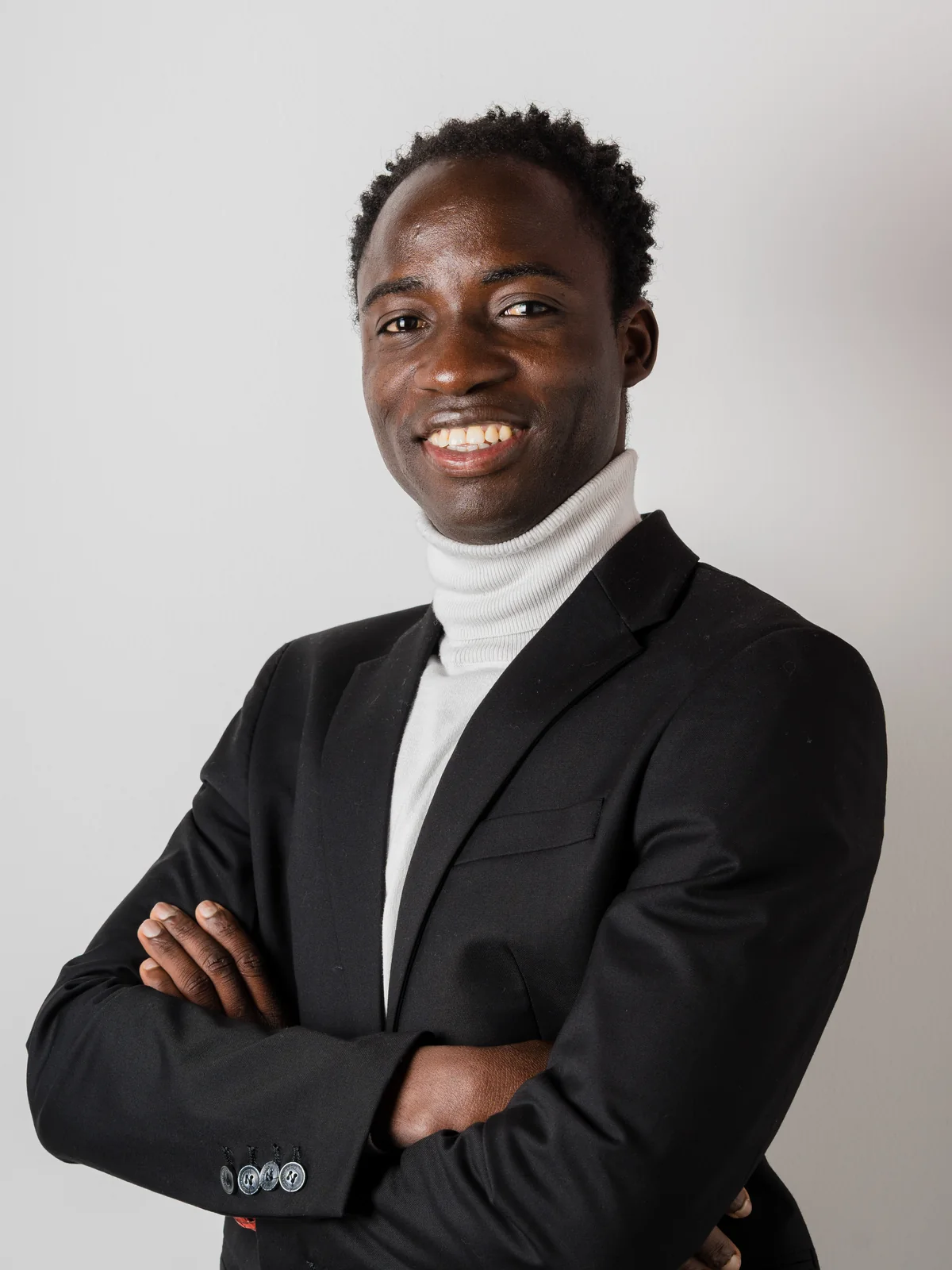 Un uomo sorridente in abito elegante, con le braccia incrociate, su uno sfondo grigio chiaro