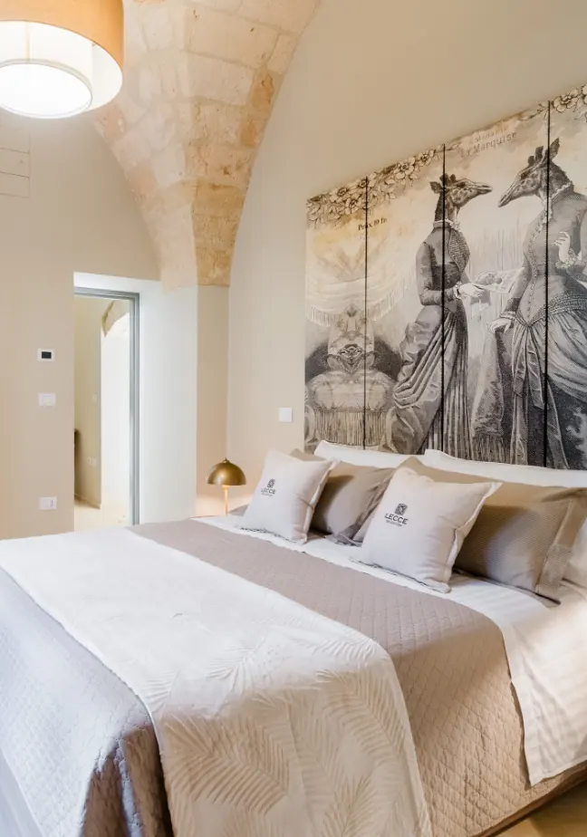 Camera da letto elegante con un grande letto, cuscini decorativi e un'opera d'arte murale che rappresenta due figure