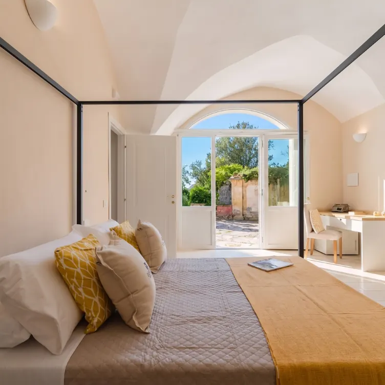 Una camera da letto luminosa con un letto matrimoniale, decorata con cuscini gialli e una scrivania, che si affaccia su un patio esterno